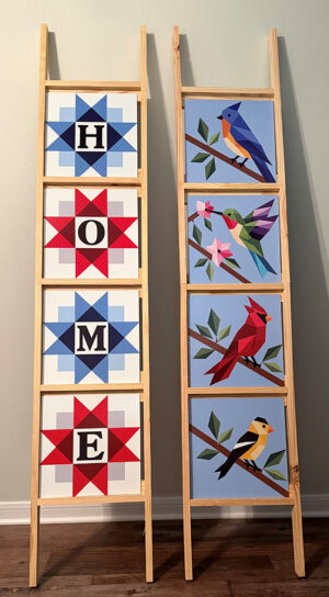 Two barn quilt display ladders holding four 12 inch panels each, one spelling HOME in red and blue star blocks, the other with bluebird, hummingbird, cardinal, and goldfinch designs